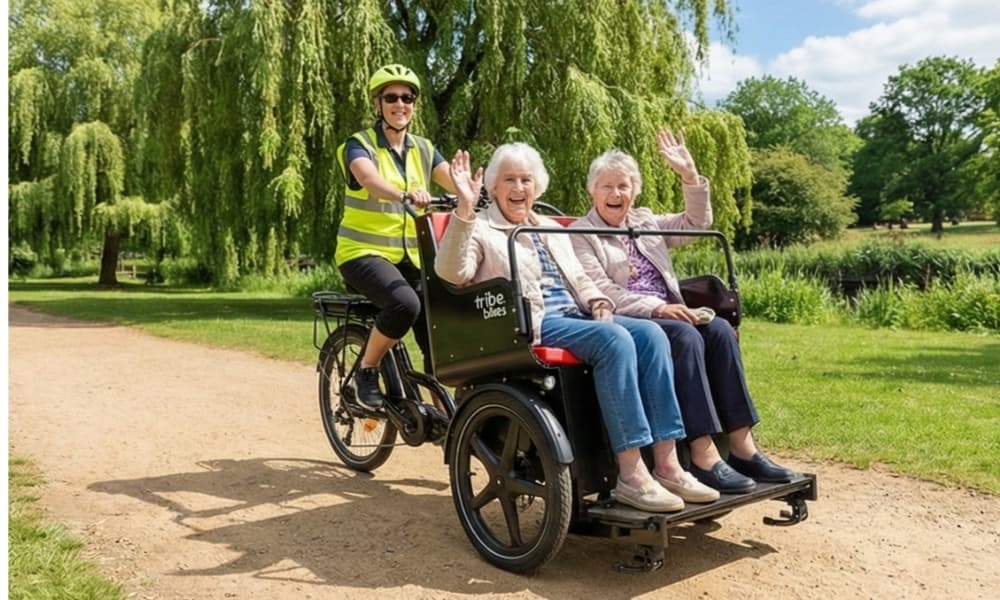 Two older women waving from a Ricky Rickshaw as a volunteer pilot rides them through a park